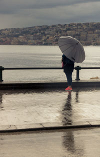 Person in front of the sea under an umbrella on a rainy day