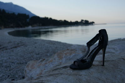 Close-up of shoes on rock at beach against sky during sunset