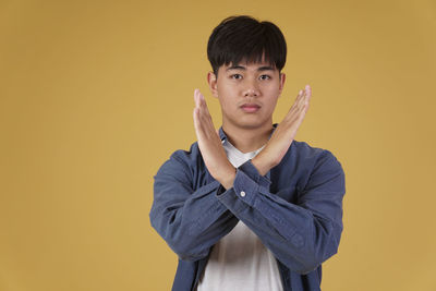 Portrait of young man standing against yellow background