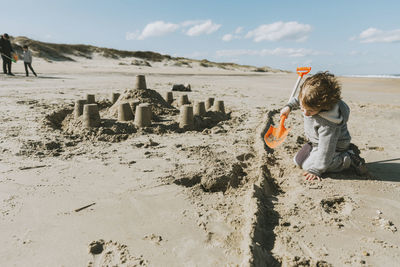 Boy making sandcastle at beach against sky during sunny day