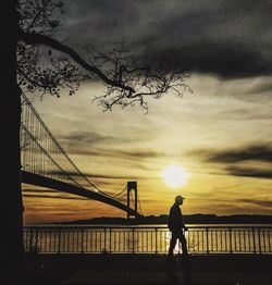 Silhouette people standing by suspension bridge against cloudy sky