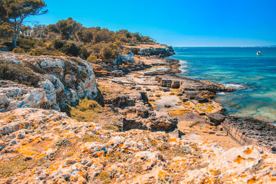 Scenic view of rocks by sea against blue sky