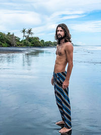 Shirtless man standing at beach against sky