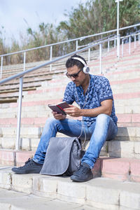 Young man using mobile phone while sitting on wall