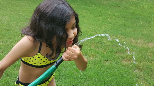 High angle view of girl drinking water from garden hose at back yard