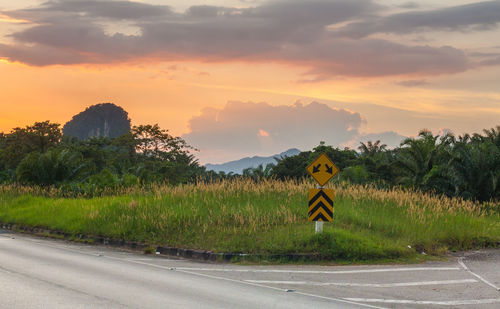 Road amidst field against sky during sunset