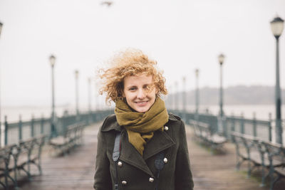 Portrait of smiling woman standing on pier by sea against clear sky