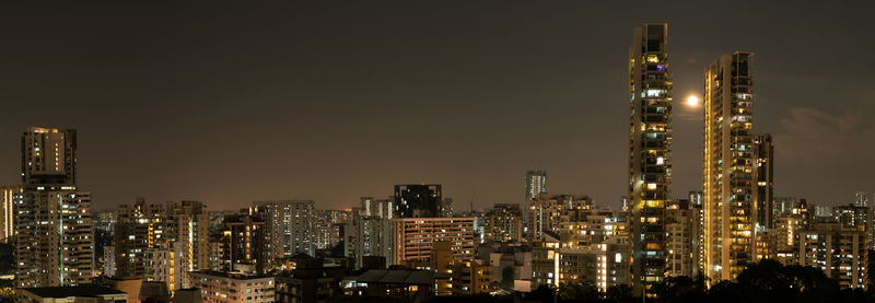 Illuminated modern buildings in city against sky at night