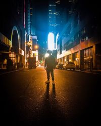 Rear view of man walking on illuminated city at night