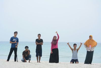 Portrait of friends standing at beach against clear sky