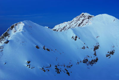 Low angle view of snowcapped mountains against clear blue sky