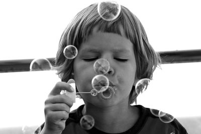 Close-up of boy blowing bubbles against sky