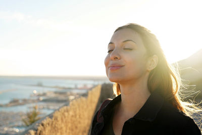 Woman with closed eyes breathing with wind on her face relaxing enjoying sun at sunset. 