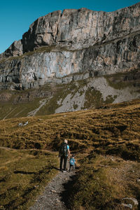 Rear view of man with son walking on trail against mountains