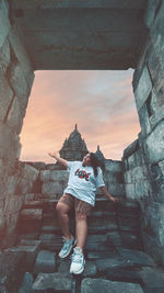 Low section of woman walking by historic building against sky during sunset