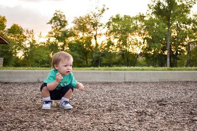 Cute baby boy crouching on field