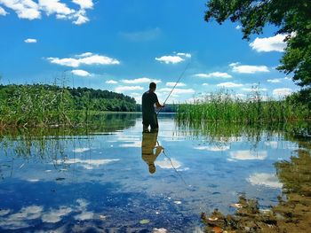 Full length of man fishing in lake against sky