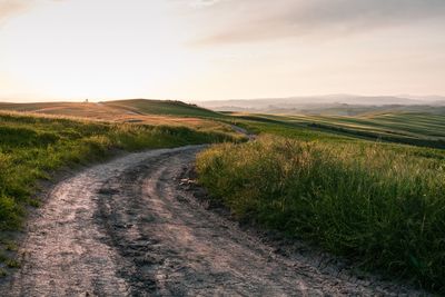 Dirt road amidst field against sky