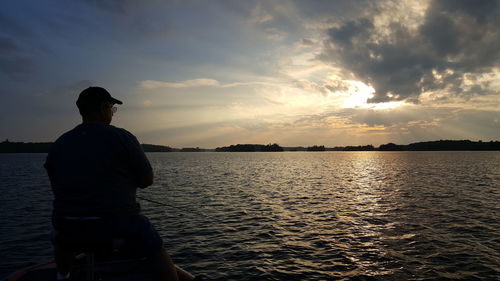 Silhouette man standing by sea against sky during sunset