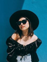 Portrait of young woman wearing sunglasses standing against wall