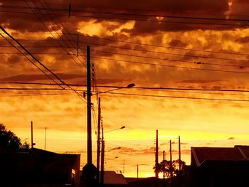 Low angle view of silhouette electricity pylon against dramatic sky