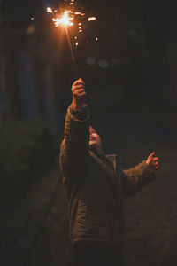 Boy celebrating holding illuminated sparkler in air 