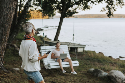 Rear view of man and woman using mobile phone while sitting on tree