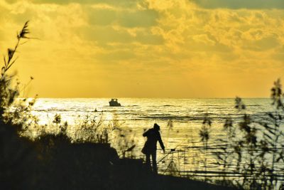 Silhouette man fishing on beach against sky during sunset