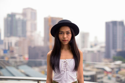 Portrait of beautiful young woman standing against cityscape