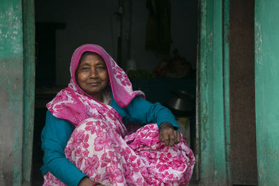 Portrait of woman wearing sari sitting at door of the house