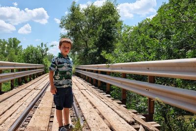 Boy standing on bridge during sunny day