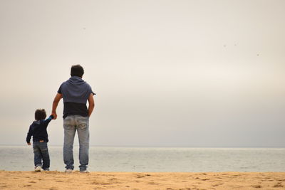 Rear view of father and son at beach against clear sky