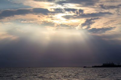 Sunlight streaming through clouds over sea during sunset