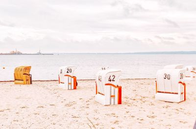 Hooded chairs on beach against sky