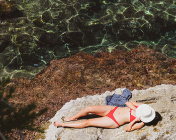 High angle view of woman wearing bikini lying on rock at beach