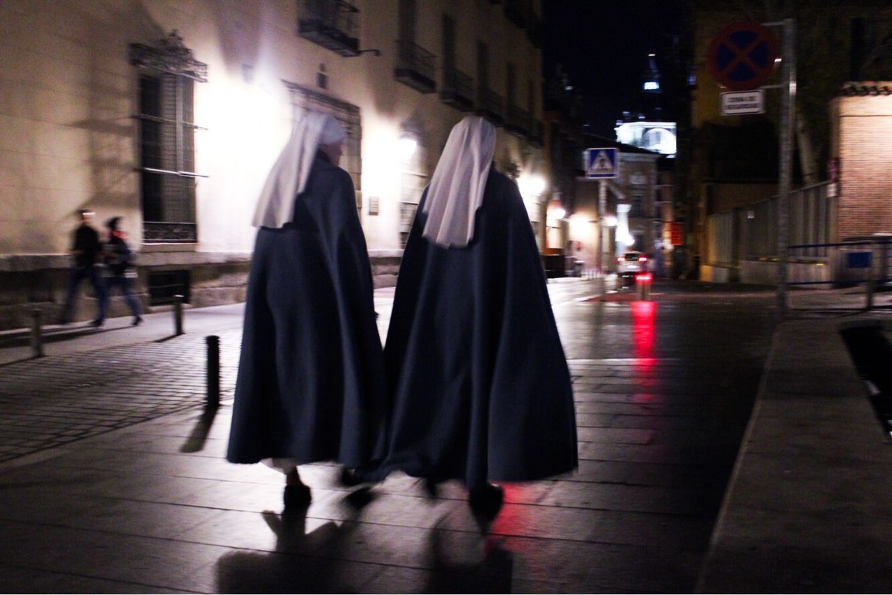 REAR VIEW OF PEOPLE WALKING ON ILLUMINATED STREET IN CITY