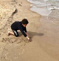 High angle view of boy writing on sand at beach