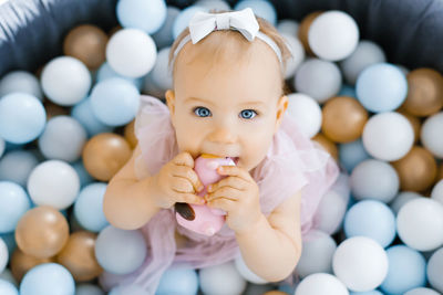 A one-year-old girl is teething, she gnaws a rubber toy, sitting in a pool with colorful balls