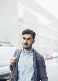 Young businessman looking away while walking on city street