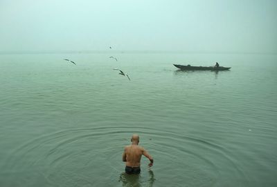 Rear view of shirtless man standing in river