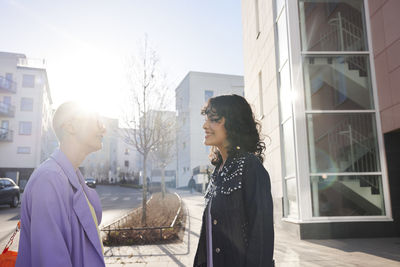 Smiling female friends or gay couple standing at road and looking at each other