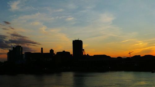 Silhouette buildings by sea against sky during sunset