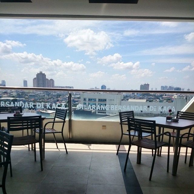 chair, sky, empty, architecture, table, built structure, indoors, absence, restaurant, seat, cloud - sky, airport, sunlight, no people, day, transportation, city, cloud, sea, railing