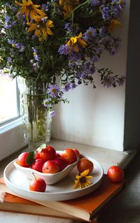 Vase with purple  flowers and orange fruit. window sill.