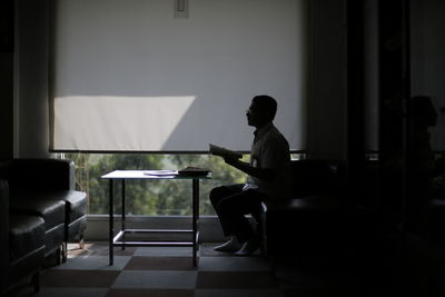 Side view of silhouette man reading book while sitting in office