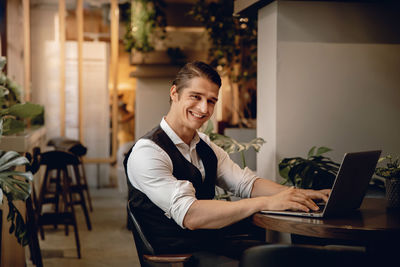 Portrait of young man using phone while sitting on table