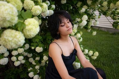 Beautiful young woman sitting by flowering plants