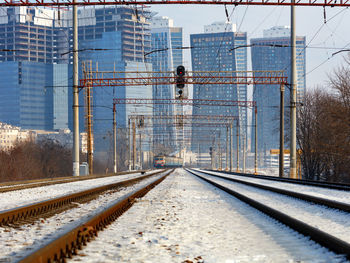 The electric train moves on rails against the backdrop of a winter cityscape.