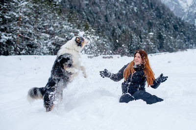 Cheerful woman playing with dog on snow covered field