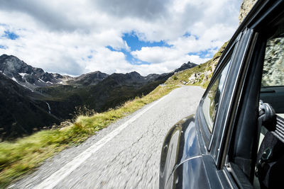 Cropped image of car on road by mountains against sky